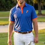 A man standing on a golf course wearing a blue floral pattern UF polo shirt with orange trim and a matching orange logo, white golf shorts, and holding a golf club.