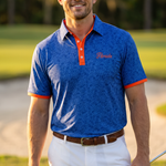 A man wearing a blue floral patterned UF polo shirt with orange trim and a matching blue patterned golf shirt, white shorts, and a brown belt, standing on a golf course and holding a golf club.