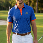 A man standing on a golf course wearing a blue floral patterned UF polo shirt with orange trim and a green Gator logo, paired with white shorts.