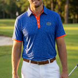 A man standing on a golf course wearing a blue floral patterned UF polo shirt with orange trim and a green Gator logo, paired with white shorts.